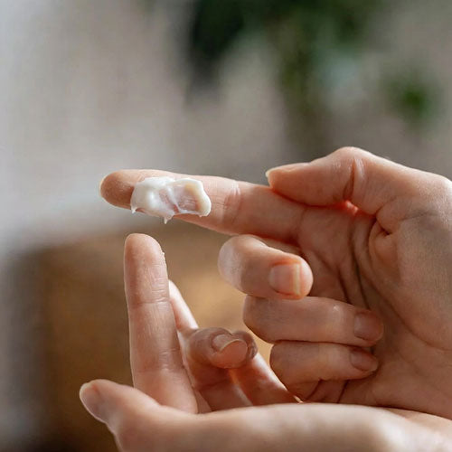 Close-up of a hand applying cream to another finger with a blurred background