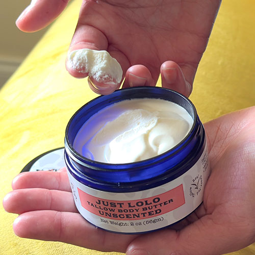 Hand holding a jar of Just Lolo body butter with a small amount on the palm.