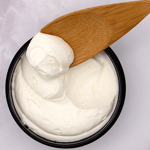 Tallow in a black container with a wooden spoon on a light gray background