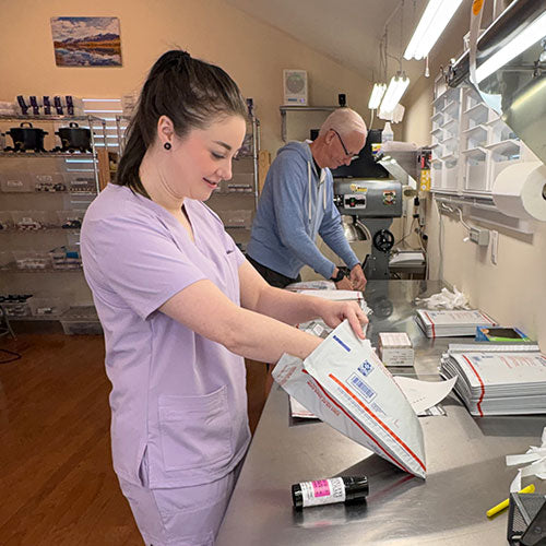 Two people in a medical or laboratory setting, one packaging a box while the other observes.