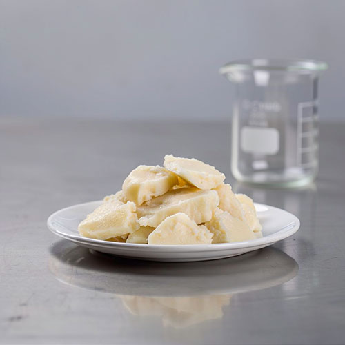 White plate with chunks of tallow on a gray surface with a beaker in the background